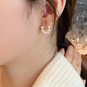 Close-up of elegant gold C-shaped earrings with rose motif and small white pearls on model