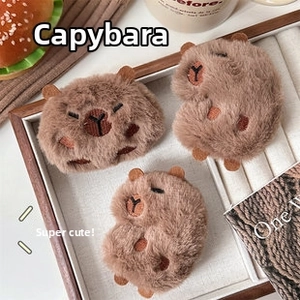 Three cute brown plush capybara pins displayed on a wooden tray with a cozy background