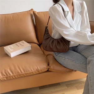 Detail of a dark brown pleated cloud bag on a leather sofa in a stylish lifestyle setting