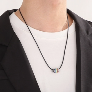 Close-up of rainbow striped cylindrical pendant on a black cord necklace worn by a model