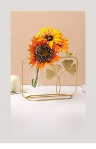Detail of golden ginkgo leaf metal frame with a glass test tube and yellow sunflowers