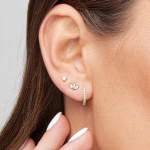 Close-up of gold ear studs and a hoop earring set with sparkling zircons on ear
