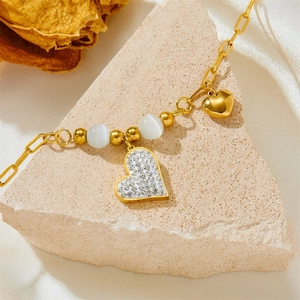 Bracelet cœur doré avec pierre œil de chat et strass sur fond de pierre beige élégant