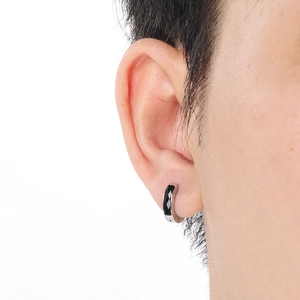 Close-up of a silver earring with black geometric inlay worn by a person on a white background