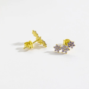 Macro shot of gold flower earrings featuring elegant purple zircon stones on white background