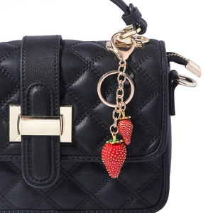 Close-up of a red strawberry charm with golden leaves on a black quilted handbag