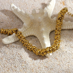 Detail of 18K gold plated rope chain bracelet on white starfish with beach sand background