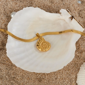Detail of gold shell pendant on snake chain over beach sand and pearl background