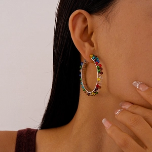 Detail view of colorful glass beads on large geometric hoop earrings worn by a model