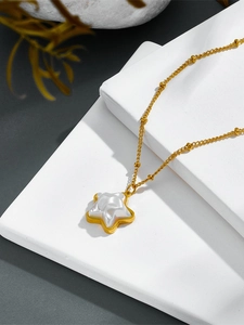 Detail of star-shaped pearl pendant on gold chain over white geometric blocks