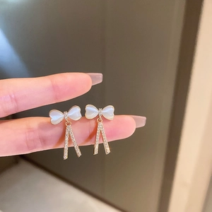 Détail de boucles d'oreilles nœud doré avec glands en cristal et fini nacré brillant