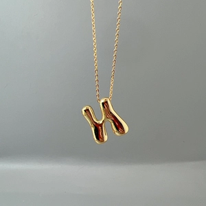 Macro shot of 3D bubble style gold letter H pendant on a polished link chain necklace