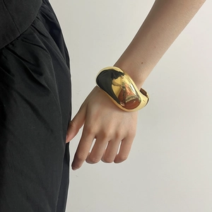 Nahaufnahme eines breiten polierten Goldarmreifs am Handgelenk für modernen Look