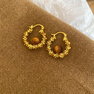 Close-up of golden hoop earrings with brown resin beads on warm brown knit fabric