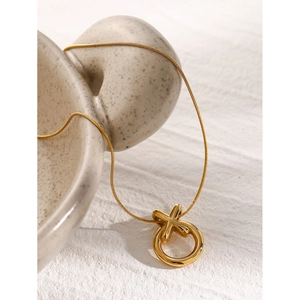 Detail of 18k gold plated XO interlocking pendant on a snake chain against ceramic art