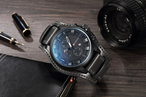 Men's quartz watch with black dial and leather strap displayed with vintage accessories