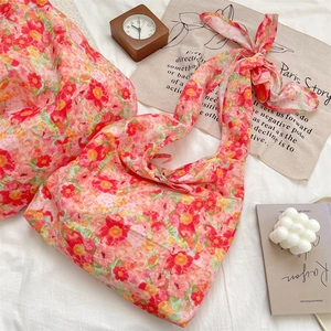 Floral print tote bag with bow straps flat laid on bed with vintage lifestyle props