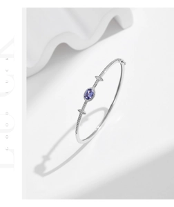Macro detail of silver geometric bangle featuring an oval purple gemstone and pavé diamonds