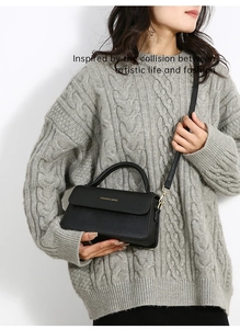 Modella che indossa una borsa nera a tracolla con fibbia dorata su maglione grigio
