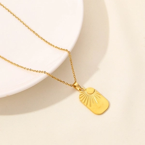 Close-up of golden sunburst pendant with fine O-chain over a minimalist white ceramic plate