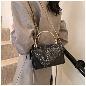 Detail view of a black sequined crossbody bag with metal handle worn by a model