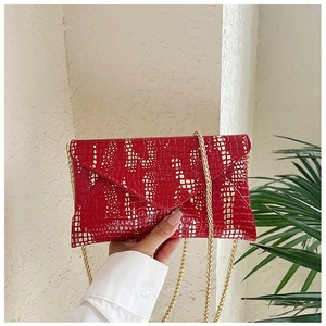 Close-up of red crocodile pattern envelope clutch bag with golden chain strap detail