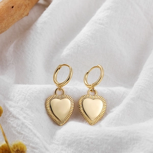 Detail of 18K gold heart earrings with textured edges and small hoops on white linen