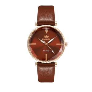 Detail of rose gold watch case with faceted glass and red radial dial on brown strap