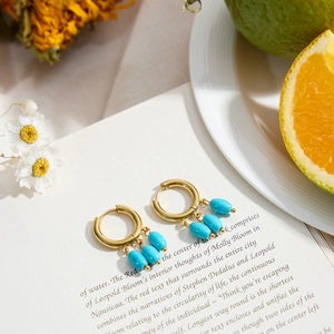 Elegant gold hoop earrings with turquoise bead drapes displayed on an open book