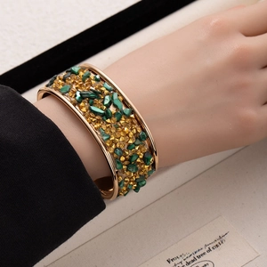 Detailed view of a wide gold cuff bracelet featuring vibrant green and amber crushed stones