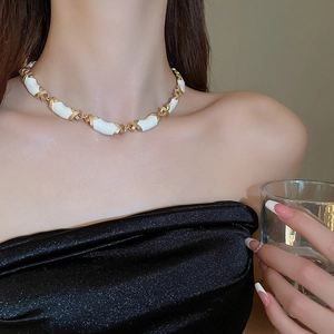 Détail du collier croisé vintage en émail blanc et doré sur le cou