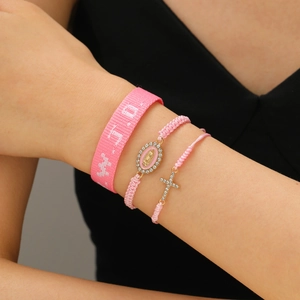 Detail of pink WWJD woven bracelet set with cross and Mary charms on a female wrist