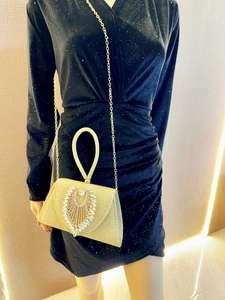 Detail of gold evening clutch bag with rhinestones and metal chain strap on evening dress
