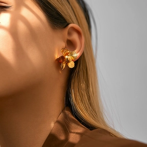 Detailed view of 18K gold flower earrings with brushed metal texture on female model