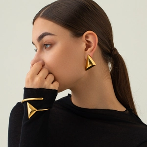 Primo piano di orecchini geometrici a triangolo placcati in oro 18k e bracciale rigido