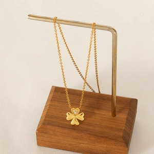Golden clover necklace with heart-shaped diamond inlay on a minimalist display stand