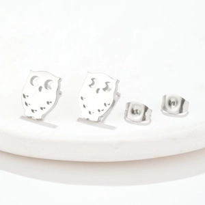 Detailed macro view of hollow owl-shaped stainless steel stud earrings with matching backings