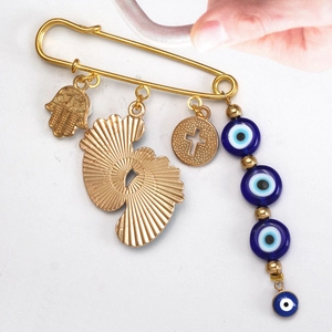 Golden Hamsa hand and blue Evil Eye charm safety pin brooch held in hand
