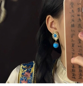 Detailed close-up of a vintage oval gold earring with blue stones worn by a model