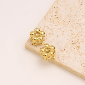 Macro shot of gold flower earrings crafted from polished metallic spheres on stone