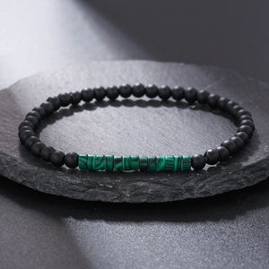 Macro detail of black matte beads and green striped malachite style stone on slate surface