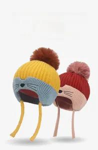 Detail of kids knitted winter hat with earflaps, fluffy pompom and cute cat face embroidery
