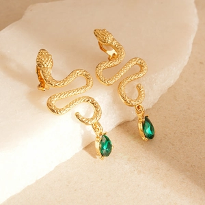 Close-up of golden snake earrings with emerald green teardrop crystals on stone