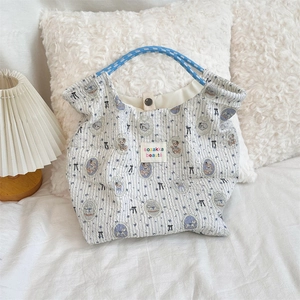 Detail of blue striped canvas tote with bear print and braided rope handle on white bedding