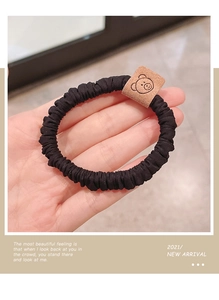 Close-up of black elastic scrunchie with a brown leather bear tag held by hand
