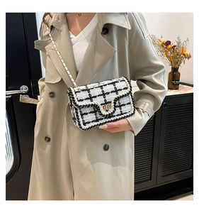 Detailopname van zwart-witte tweed geruite crossbodytas met gouden metalen draaisluiting