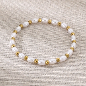 Détail de bracelet en perles d'eau douce et acier inoxydable doré sur tissu beige