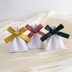 Close-up of three white velvet drawstring bags with gold, pink, and dark green silk ribbons