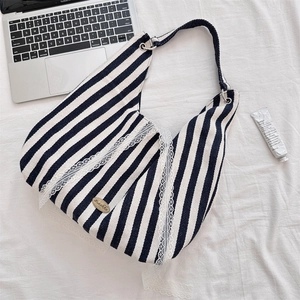 Détail du sac hobo à rayures bleues avec dentelle et logo métallique sur un drap blanc
