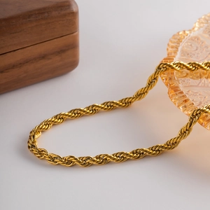 Collier chaîne torsadée dorée posé sur une assiette en verre ambré avec reflet brillant